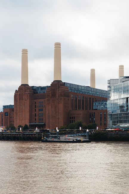 Photograph of Battersea Power Station under construction or renovation, with multiple cranes positioned around the structure working on the building's exterior. The building features tall yellow smoke